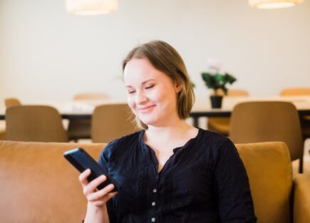 Koas resident in Palstatie lounge scrolling on her phone sitting on sofa.